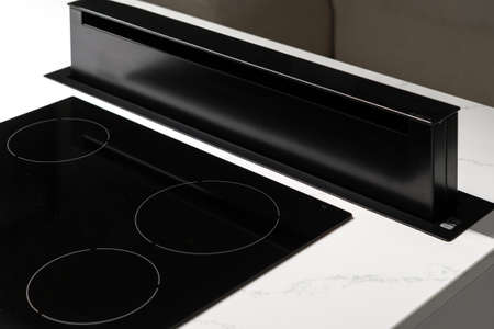 State of black ceramic induction stove top with retractive exhaust device on clean countertop with white surface, convenient modern kitchen technology with nobody in picture, close upの写真素材