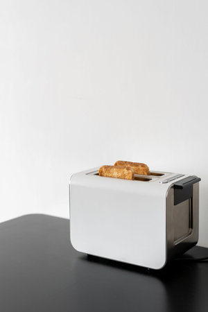 Vertical shot of white modern toaster with slices of bread inside on black counter with white background in kitchen, copy space for textの写真素材