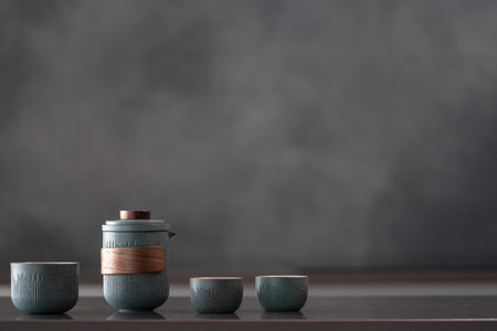 Glossy reflective countertop with nice ceramic blue teapot set, three small cups, brewing tea for...