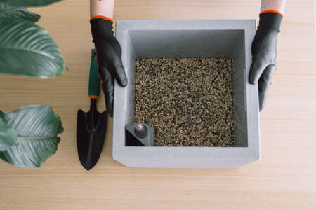 Image shot from above of gardener hands in black gloves holding smart plant pot prepared for further planting field on half with drainage of minerals and water level indicator fixed in corner insideの写真素材
