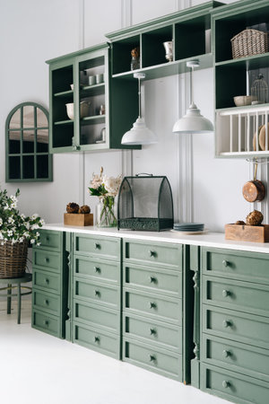 Kitchen counter with lots of drawers, white surface with flowers in jar and different devices on top...
