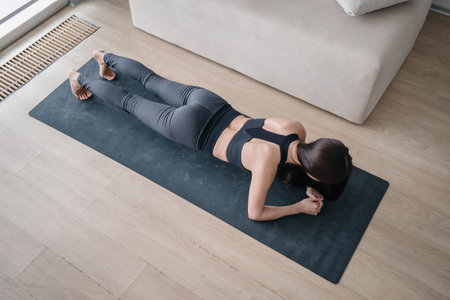 Above view of young fit woman wearing modern sportswear during endurance training at home, standing...