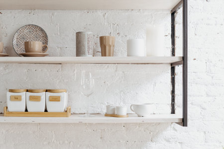 Closeup of wooden shelf at white kitchen. Ceramic cup, plate, dish, kitchenware at wood furniture....