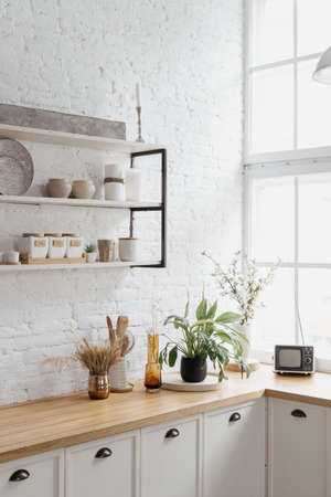 Home kitchen interior, closeup of modern decor. Minimalistic rustic house with indoor white brick wall, contemporary apartment design. Wooden tabletop under shelf with ceramic kitchenware.の写真素材