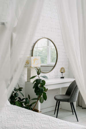 Bedroom interior, closeup at white room design. Nobody at home, vertical shot of scandinavian apartment decor. Furniture with curtain, modern design with table, mirror, chair near bed.の写真素材
