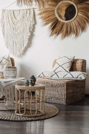 Natural material furniture and macrame on white wall in living room interior in bali or indonesian style. Vertical view of comfortable armchair with cushions near bamboo coffee table with home decorの写真素材