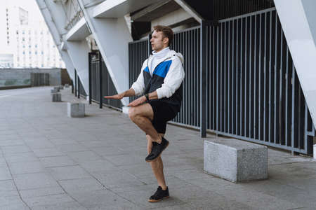 Healthy lifestyle and everyday sport concept. Side view of athlete jumping up, doing breathing exercise in cardio training. Sporty man workout outdoor in cityの写真素材