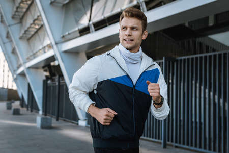 Concept of morning cardio and daily exercise. Waist up portrait of strong runner. Football player jogging outdoor, looking aside. Sportsman doing training in city, prepare his body to the competitionsの写真素材