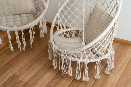 Two comfortable hanging rope swings with soft cushions over wooden laminate or hardwood parquet floor. Modern bedroom or living room interior with copy space. Recreation, relaxation conceptの写真素材