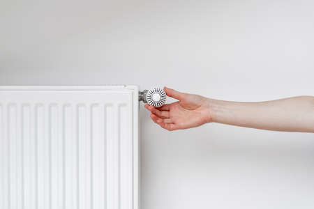 Cropped view of woman hand adjusting thermostat on white heating radiator. Consumption of natural resource, saving energy and warm home conceptの写真素材