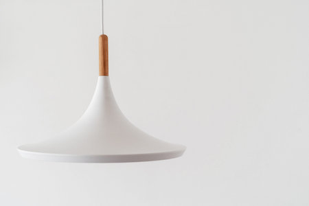 Modern white ceiling lamp hanging against copy space wall in bright living room with minimalist interior design. Concept of electric equipment and illumination in bedroomの写真素材