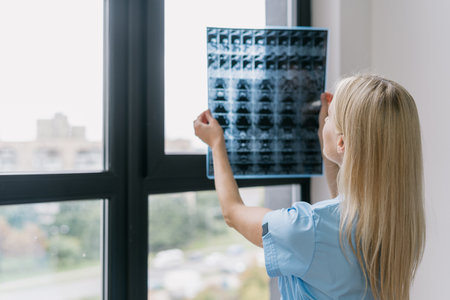 Healthcare concept. Back rear view of general practitioner in medical uniform standing near window, looking at x ray picture of patient. Doctor diagnostic disease, checking mri scan at private clinicの写真素材