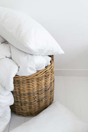 Household, hotel service and home concept. Dirty bedding for laundry packing in wicker basket. Vertical view of clean sheets, white pillow and blanket or duvet in comfort bedroom, close upの写真素材