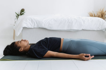 Side profile view of african american girl in sportswear lying on yoga mat, resting after sport...