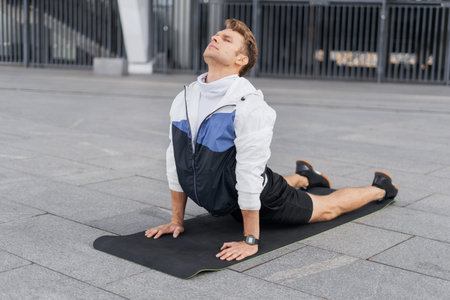 Side view of young athlete practicing yoga, lying in Cobra pose, doing back bend stretching...