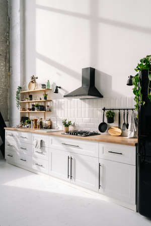 Bright modern kitchen interior design with white furniture, shelves, refrigerator, hood and household appliances and decorations. Neutral wall and floor at dining roomの写真素材