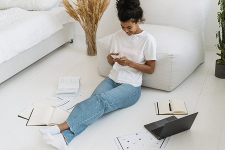 High angle view of smiling young millennial girl using online app on her modern smartphone, sitting...