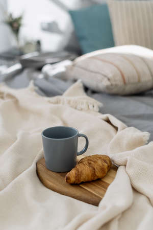 Vertical view of wooden breakfast tray with coffee cup and yummy baked growing in cozy bedroom. Concept of lazy weekend morning at home with delicious food in bedの写真素材
