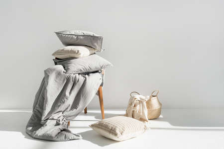 Plaid in wicker basket, clean blanket, linen bedding, cotton sheets, pillow, cushion and duvet with natural material on chair after laundry, copy space. Washing, housekeeping, hotel service conceptの写真素材