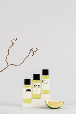 Advertising concept. Set of hotel toiletry with shower gel, lime soap, citrus shampoo and hair conditioner standing on podium against light gray background with copy spaceの写真素材