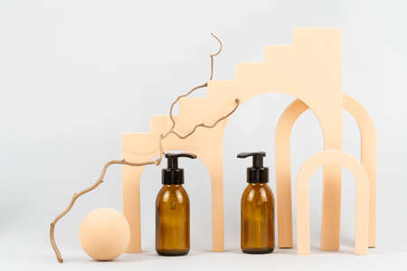 Composition with geometric shapes, dry plant and natural body care cosmetic products. Glass zero waste bottles with pump standing on light gray and copy space background. Advertising conceptの写真素材