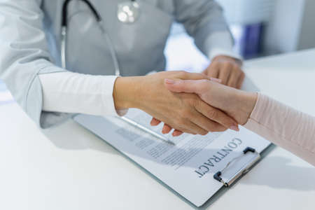 Commercial medicine, coverage policy concept. Cropped view of doctor shakes hands with the patient after signing medical insurance contractの写真素材