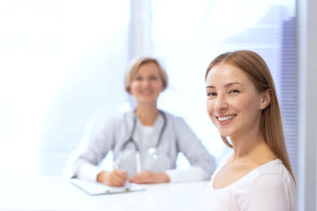 Happy and healthy patient looking at camera, smiling wide, sitting against doctor on blurred background. Concept of visiting the clinic, treatment, healthcare and health check upの写真素材