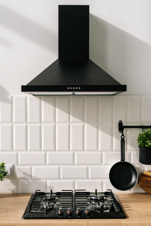 Closeup of modern kitchen interior in white and black tones with frying pan, stove and extractor...