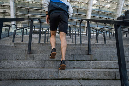 Sport exercise and healthy lifestyle concept. Low angle, cropped view of sportsman running on steps, training outdoors, warm up his body, getting ready to daily workout in the city, back rear shotの写真素材