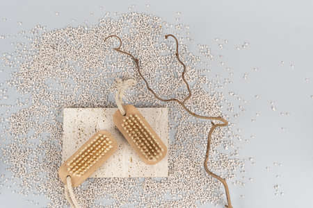 Flat lay view of two small wooden nail brush lying on scattered sand close to natural wood brunch. Manicure, pedicure scrubbing and hand care concept. Objects on light gray background with copy spaceの写真素材