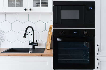 Cropped view of modern Skandinavian style kitchen with white furniture and black appliances. Pleasant place for cooking. Luxury apartment for saleの写真素材