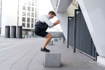Do your best. Concept of dynamic exercise and cardio training in sport. Profile and full length view of young sportsman jumping up on box, warm up body, getting ready to run on the streetの写真素材