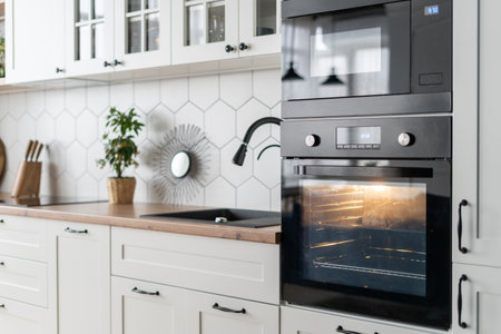 Side view of contemporary black oven kitchen interior design. Stylish white wood furniture surface with appliances and decor. Cozy place for cooking. Baking processの写真素材