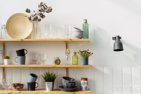 Beautiful wooden shelves with kitchen utensils and decor closeup. Cozy environment in luxury dining room. Contemporary jars and bottles. Diversity of cups and platesの写真素材