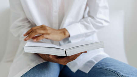 Cropped view of african girl reading book in cozy room. Process of enjoying literature novel. Modern literature addiction. Teenagers hobby and activityの写真素材