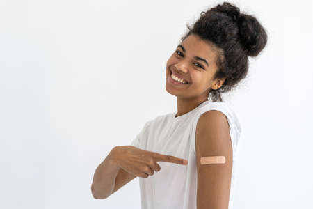 Portrait of happy african teenager pointing at plaster on arm on white background. Covid-19 vaccination concept. Healtcare idea. Virus protectionの写真素材