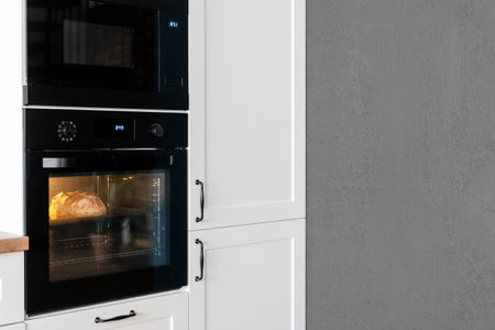 Side cropped view of stylish black oven in kitchen interior design. Food baking process....