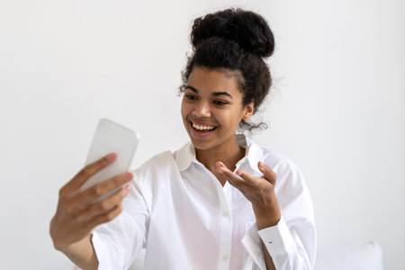 Positive african american millenial lady using smartphone to make video call. Communication during...