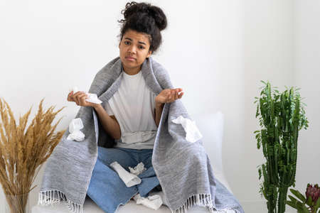Sad African American girl suffering from cold or flu with handkerchief and plaid. home treatment concept. health care and medicine. lady feeling badの写真素材