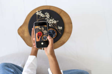High above view of afro american girl taking food photo on smartphone camera at home. Concept of food blogger, influencer. Teenagers hobby and activityの写真素材