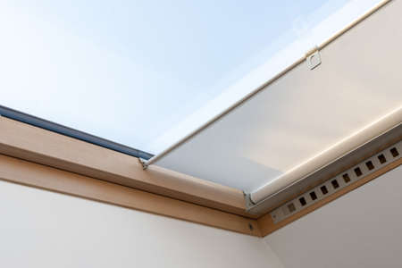Close up view of roller blinds cover double glazing attic or mansard window in wooden frame. Modern apartment with room under roof with skylight and sky viewの写真素材