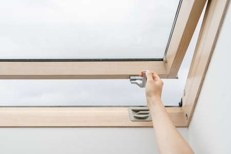 Concept of energy efficient house. Woman hand open or closed attic window in wooden frame. Comfortable room under roof. Building construction and renovation processの写真素材