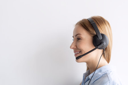 Side view of attractive woman with headset standing near white wall. remote work concept. technical...