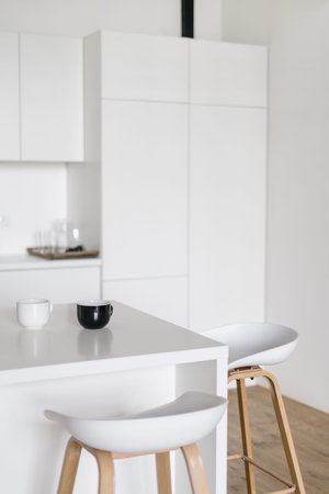 Side view of modern kitchen interior design with bar chairs. cups on table. Spacious and bright...