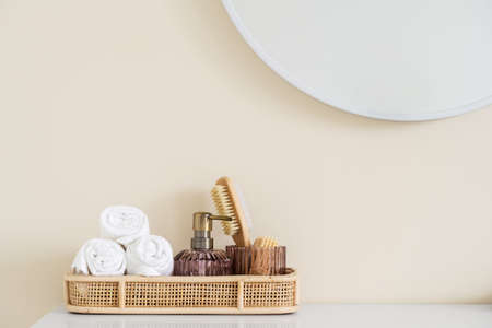 Bamboo tray with rolled face or hand towels, soap dispenser bottle and small wooden brush standing on makeup table in bathroom at hotel. Concept of self and skin careの写真素材