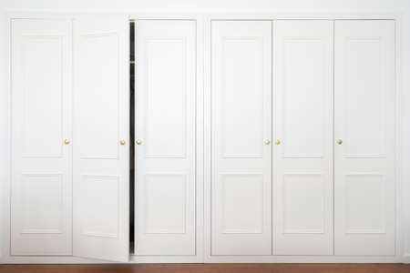 Front view of large white wardrobe in american classic style with ajar door in light room. Advertising of ergonomic furniture and spacious closet at modern apartment interiorの写真素材