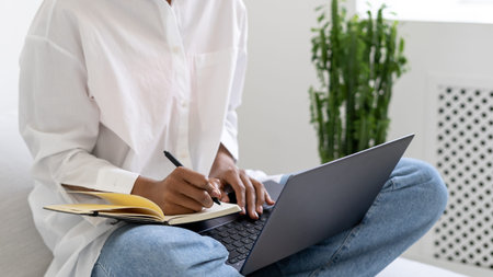 Cropped view of african american lady holding laptop and making notes. Distance education process...