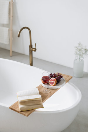 High above view of ceramic white bathtub with copper faucet. Fruits, wine and open book on wooden...