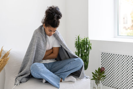 Portrait of young afro american girl covering with blanket suffering from chills. Medicine and...