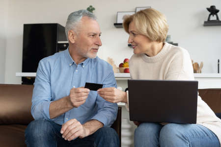 Married couple paying for shopping with credit card. Middle aged woman with laptop help her husband make deposit fee, repayment of loan debt or money transfer on internet. online banking conceptの写真素材